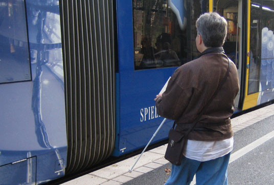 An der Straßenbahnhaltestelle: Einstieg in die Bahn, doch zunächst Aufsuchen der Tür mit dem Langstock!