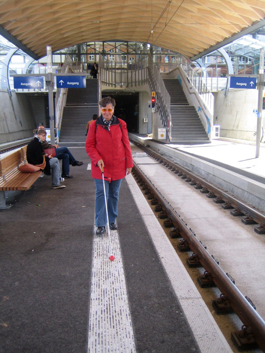 Nutzung von taktilen Leitstreifen zur Orientierung mit dem Langstock auf dem Bahnsteig.