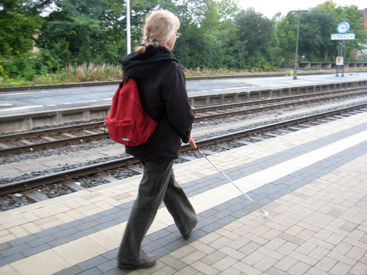 Nutzung von taktilen Leitstreifen zur Orientierung mit dem Langstock auf dem Bahnsteig.